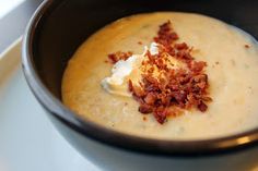 a black bowl filled with soup on top of a white plate and topped with bacon