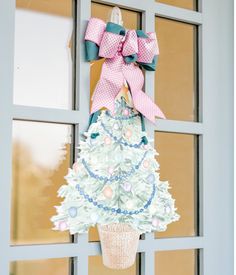 a decorated christmas tree hanging from the side of a door with a pink bow on it