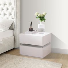 a white nightstand with flowers on it next to a bed