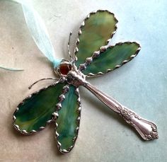 a green flower shaped brooch with a blue ribbon around it's neck and an orange stone in the center