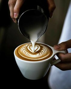 someone pours milk into a cup of latte art with a heart pattern on the foam