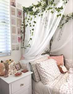 a white bed sitting next to a window covered in green vines and flowers on top of it