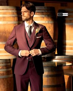 a man in a purple suit standing next to some wooden barrels and looking at the camera