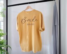 a t - shirt that says bride on it hangs from a clothes hanger next to a potted plant