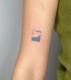 a woman's arm with a small blue sky and clouds tattoo on the back of her left arm