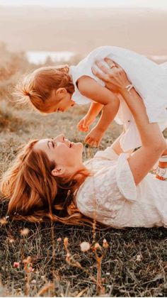 a woman holding a baby up in the air while laying on her stomach and smiling