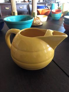 a yellow pitcher sitting on top of a wooden table next to other bowls and plates