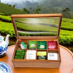 a wooden box filled with teas on top of a table next to a cup and saucer