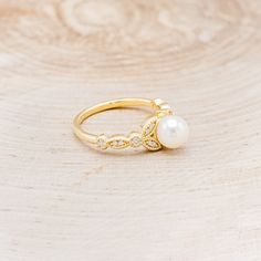 a pearl and diamond ring sitting on top of a wooden table