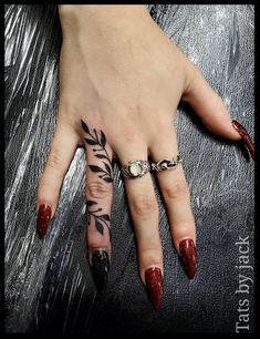 a woman's hand with red fingernails and tattoos on her left thumb, holding onto a ring