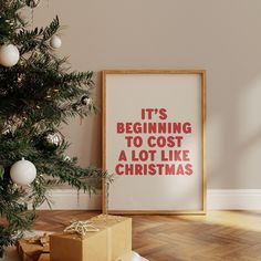 a christmas tree with presents under it next to a framed poster that says it's beginning to cost a lot like christmas