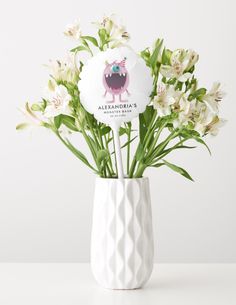 a white vase filled with lots of flowers on top of a table next to a sign