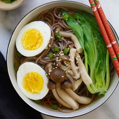 a bowl filled with noodles, mushrooms and eggs on top of a white table next to chopsticks