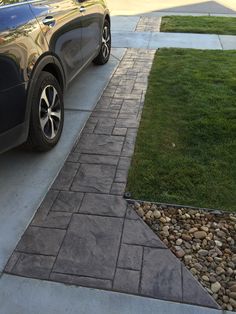 a car parked on the side of a road next to a grass covered yard and driveway