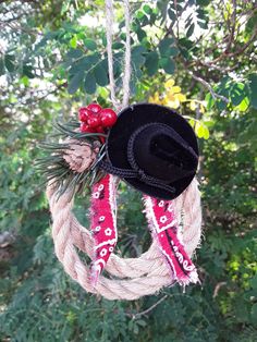 a cowboy hat hanging from a rope with berries and pine cones on the end, surrounded by greenery