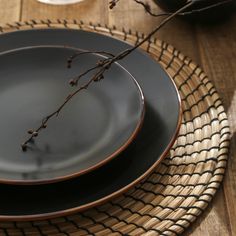 a black plate with two brown rims sitting on a woven place mat