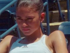 a woman holding a tennis racquet on top of a tennis court next to bleachers