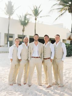 a group of men standing next to each other on top of a sandy beach in front of palm trees