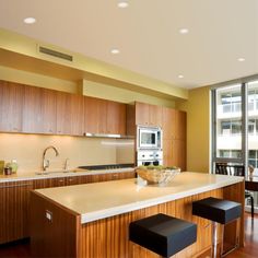 a kitchen with wooden cabinets and white counter tops next to a large window overlooking the city