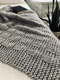 a bed covered in a gray knitted blanket next to a potted plant