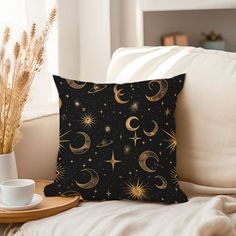 a black pillow with gold stars and crescents on it next to a coffee cup