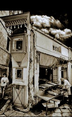 an old building with people standing outside and looking at something on the ground in front of it