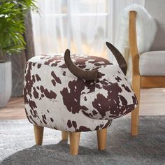 a cow footstool sitting on top of a rug next to a chair and potted plant