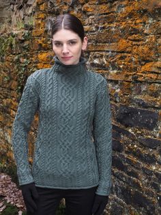 a woman standing in front of a brick wall wearing a green sweater and black gloves