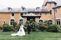 a bride and groom walking in front of an old mansion