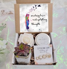 an open box with some flowers and other items in it on a table next to a card