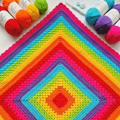 a crocheted blanket with yarn and balls of thread on the table next to it