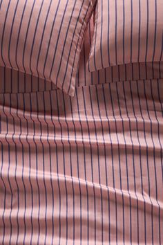 the bed is made with pink and blue pinstripe sheets, pillows, and pillow cases