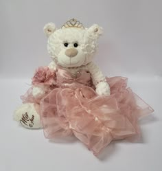 a white teddy bear wearing a pink dress with a tiara on it's head