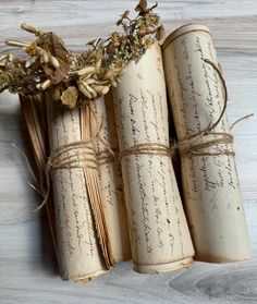 four rolled up books tied with twine and dried flowers on a white wooden surface