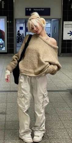 a woman with blonde hair wearing white pants and a brown sweater is standing in an airport