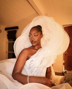 a woman in a white dress sitting on a bed wearing a veil over her head