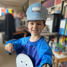 a young boy wearing a blue shirt and hat holding a paper plate with a smiling face on it