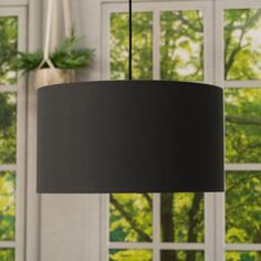 a black lamp hanging from a ceiling in front of a window with green trees outside