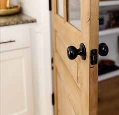 an open wooden door with black knobs in a kitchen