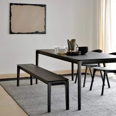 a black table and bench in a white room with a large painting on the wall