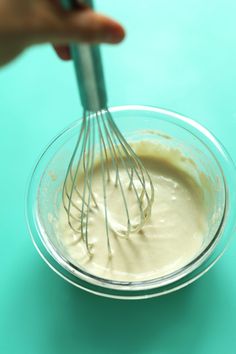 a whisk in a glass bowl filled with batter on a blue table top