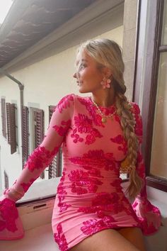 a woman in a pink dress sitting on a window sill