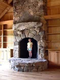 a young boy standing in front of a stone fireplace