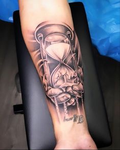 a man with a black and grey tattoo on his arm holding an hourglass in front of him