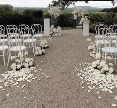 an outdoor ceremony set up with white chairs and flower petals on the ground in front of it