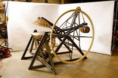 an old spinning wheel sitting on top of a wooden table next to a white wall