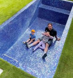 two children and an adult are sitting in a swimming pool with blue tiles on the floor