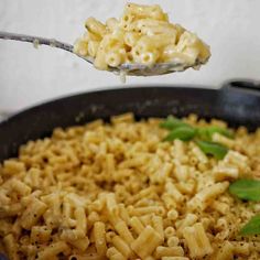 a spoon full of macaroni and cheese is being lifted from a skillet