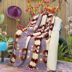 a purple and white blanket sitting on top of a wooden bench next to flowers in a potted planter