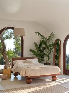 a bed sitting in the middle of a bedroom next to two large arched windows and a potted plant